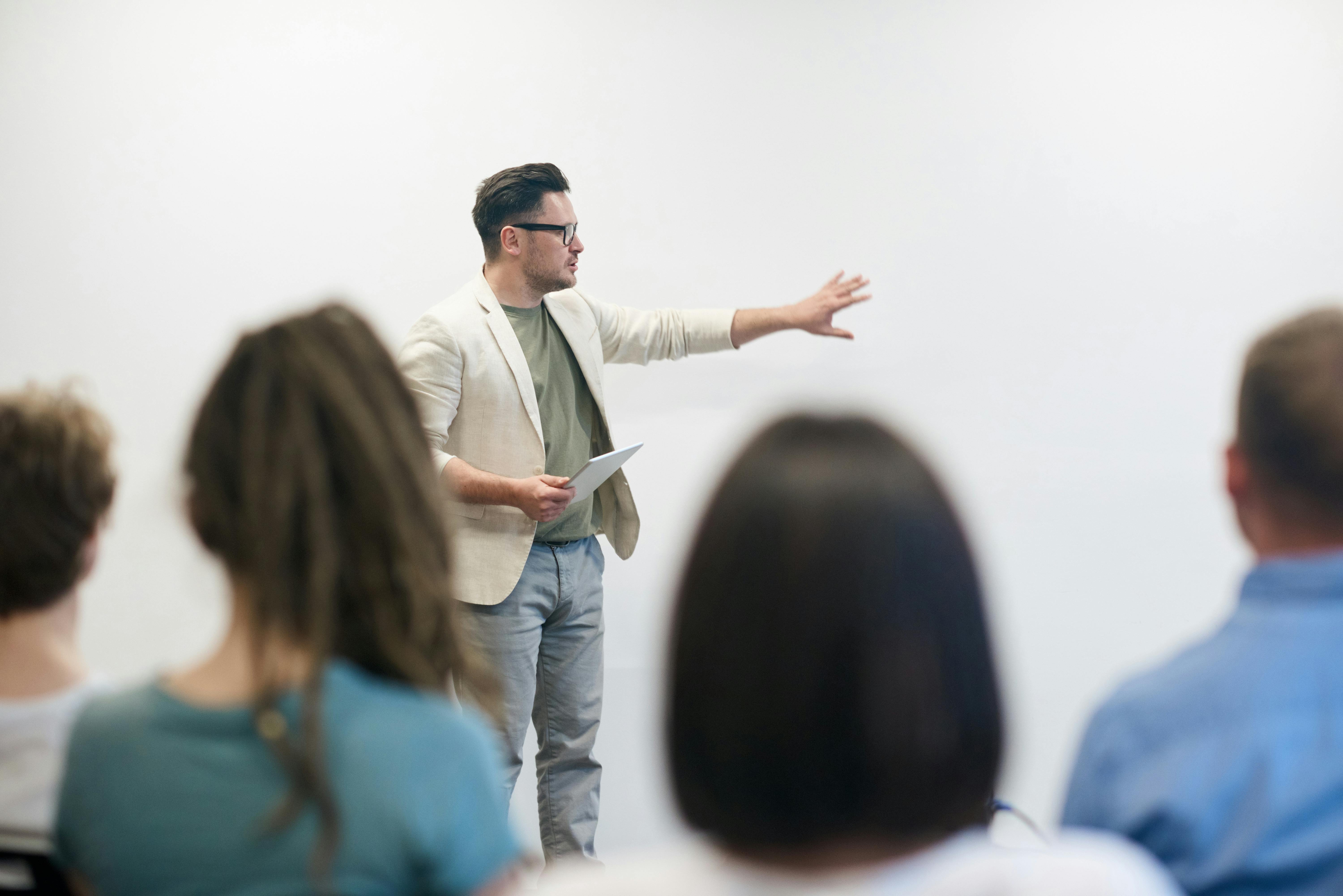Man standing in front of a class giving a presentation and pointing towards a whiteboard